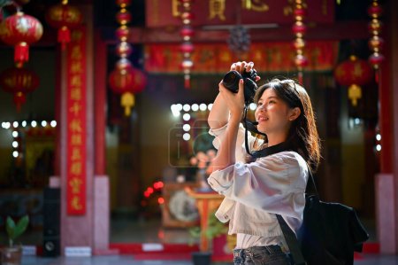 Happy and joyful young female tourist enjoys taking photos in a beautiful Chinese temple on her vacation.