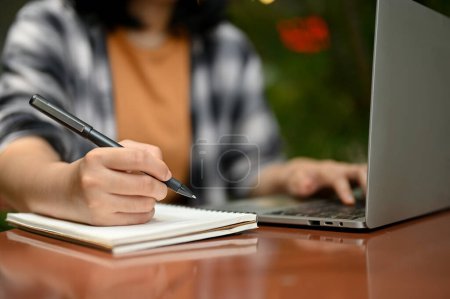 Cropped image of a young Asian female college student or a freelancer working on her tasks on laptop at an outdoor cafe.