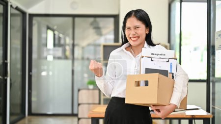 Foto de Sonriendo y emocionada joven trabajadora de oficina asiática está celebrando su renuncia, llevando sus cosas personales, feliz de dejar su trabajo o cambiar de puesto de trabajo. - Imagen libre de derechos