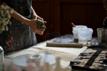 Close-up image of a master clay artist or potter kneading raw clay at his desk in the creative dark studio.