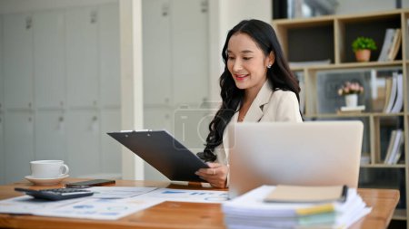 Téléchargez les photos : Une femme d'affaires asiatique millénaire attrayante ou gestionnaire féminin lit des rapports d'affaires à son bureau dans le bureau. - en image libre de droit