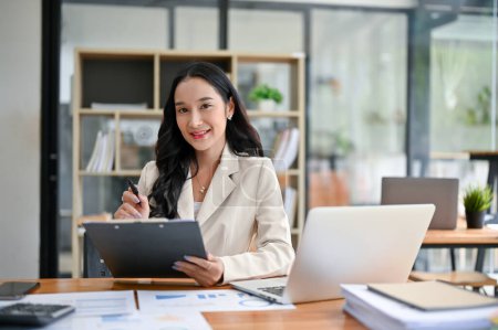 Téléchargez les photos : Portrait d'une belle femme d'affaires asiatique millénaire ou d'une directrice exécutive assise à son bureau avec un rapport d'entreprise et son ordinateur portable. - en image libre de droit