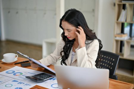 Téléchargez les photos : Une femme d'affaires asiatique millénaire professionnelle et réfléchie lisant et examinant les rapports d'entreprise à son bureau dans le bureau. - en image libre de droit