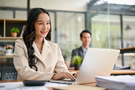 Téléchargez les photos : Une belle et professionnelle femme d'affaires asiatique millénaire utilisant son ordinateur portable pour gérer ses tâches, travaillant à son bureau dans le bureau de co-working. - en image libre de droit
