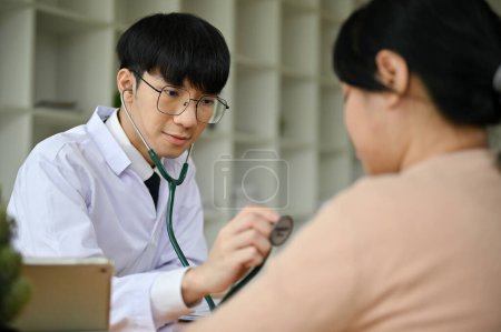 Foto de Un médico asiático milenario feliz y profesional utiliza un estetoscopio para examinar los latidos del corazón de una paciente femenina en el hospital. concepto de atención sanitaria - Imagen libre de derechos