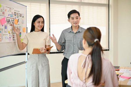Dwóch profesjonalnych azjatyckich programistów prezentuje swój nowy projekt swojemu zespołowi podczas spotkania. startująca firma technologiczna, UI, UX