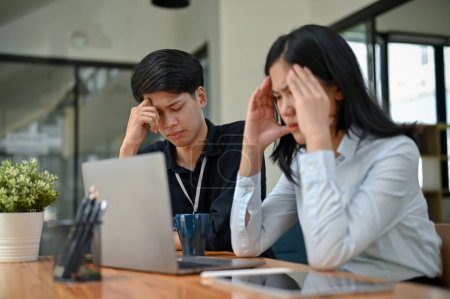 Two serious and stressed Asian office workers are focusing on their co-project together, planning and finding solutions to their project problems.