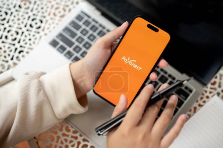 Photo for Chiang Mai, Thailand - Oct 19 2023: close-up image of a woman using a Payoneer application on her Iphone14 at her modern office desk. Payoneer logo on Iphone14 screen - Royalty Free Image