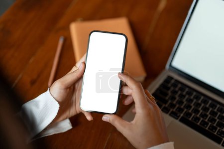 Photo for Top view of a woman using her smartphone while sitting at her working desk. A white-screen smartphone mockup. close-up image - Royalty Free Image