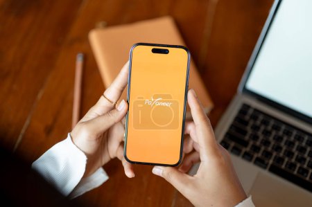 Photo for Chiang mai, Thailand - Oct 24 2023: A woman using Payoneer application on her Iphone14 at her desk. Payoneer logo on Iphone14 screen. - Royalty Free Image