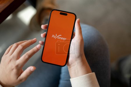 Photo for Chiang Mai, Thailand - Oct 31 2023: Close-up image of a woman using Payoneer on her IPhone14 while sitting indoors. Payoneer logo on IPhone14 screen. Financial service platform - Royalty Free Image