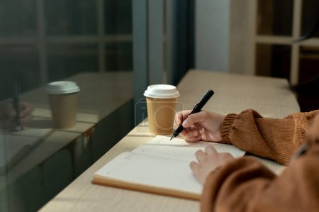 Photo for Close-up side view image of a woman writing something in her book, working remotely in a coffee shop on the weekend. People and lifestyle concepts - Royalty Free Image