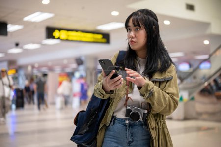 Téléchargez les photos : Une jeune voyageuse asiatique sérieuse en solo ou en sac à dos se promène à l'aéroport, à la recherche de son comptoir d'enregistrement. départ, vol intérieur, vacances - en image libre de droit