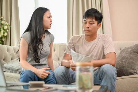 An unhappy and stressed Asian wife is arguing with her husband about unexpected expenses and high domestic bills on the sofa in the living room. spouses quarreling at home. family bankruptcy