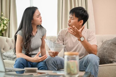 Unhappy, stressed Asian spouses are sitting on a couch, arguing about unexpected high household bills and credit card invoices. family bankruptcy, debt, lack of finances