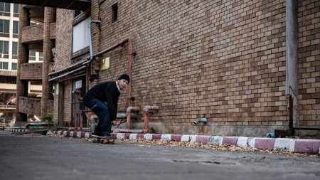Ein cooler, aktiver asiatischer Skater in stylischer Hipster-Kleidung fährt auf der Straße Skateboard und genießt das Skateboardfahren im Freien.