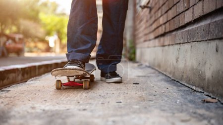 Eine Nahaufnahme zeigt die Füße eines männlichen Skaters, der auf einem Skateboard auf der Straße fährt. Aktive Skater-Beine beim Skateboarden auf einer Straße in der Stadt nicht wiederzuerkennen.