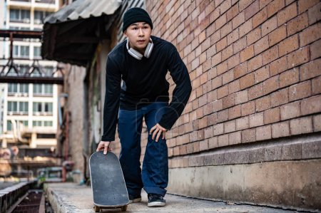 A stylish, hipster Asian male skater in fashionable clothes is practicing skateboard on the footpath, skateboarding on the city street. extreme sports concept