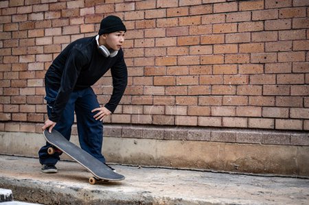 A stylish, hipster Asian male skater in fashionable clothes is practicing skateboard on the footpath, skateboarding on the city street. extreme sports concept
