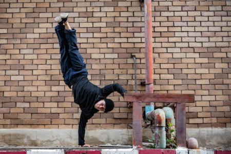 A professional, active Asian male hip-hop breakdancer is dancing on the street in the city, standing on one hand, showcasing his talented movements.