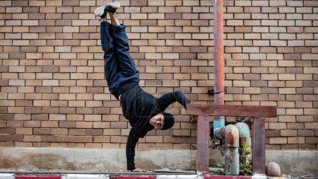 Un profesional y activo bailarín asiático de hip-hop está bailando en la calle de la ciudad, de pie por un lado, mostrando sus talentosos movimientos.