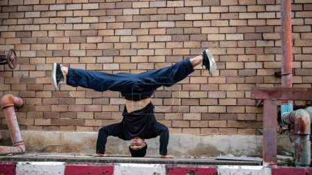 A cool, energetic Asian male b-boy hiphop breakdancer is showcasing his talented movements on the street, doing freeze pose, enjoying b-boy dancing outdoors.