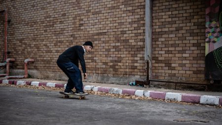 Ein cooler asiatischer Hipster in modischer Kleidung und Mütze skateboardet auf der Straße in der Stadt, fährt im Freien Skateboard und balanciert seinen Körper auf einem Skateboard.