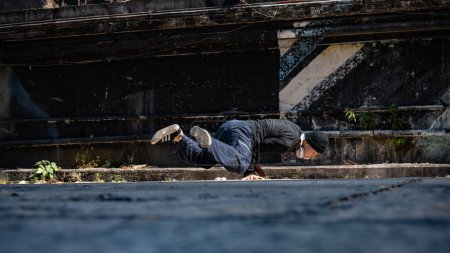 A cool, talented, professional Asian male hiphop dancer is spinning his body with hands, breakdancing on the street in an abandoned street in the city.