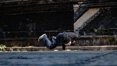 A cool, talented, professional Asian male hiphop dancer is spinning his body with hands, breakdancing on the street in an abandoned street in the city.