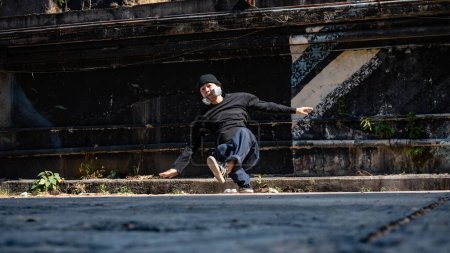 An energetic and professional Asian male hiphop breakdancer in fashionable clothes is breakdancing on the abandoned street, enjoying the rhythm.