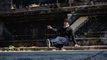 An energetic and professional Asian male hiphop breakdancer in fashionable clothes is breakdancing on the abandoned street, enjoying the rhythm.