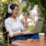 A happy Asian woman is having an online meeting with her colleagues, working outdoors at her green backyard garden. working remotely concept