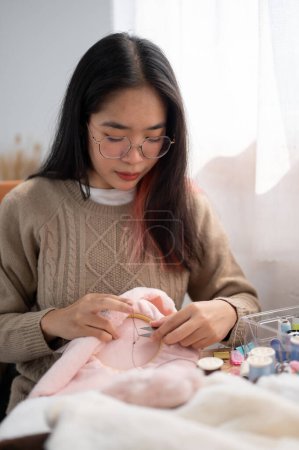 Une belle femme asiatique se concentre sur la couture à la main d'un motif sur un tissu sur un cadre de broderie, l'artisanat d'articles faits à la main à la maison. sertissage, tailleur, couture