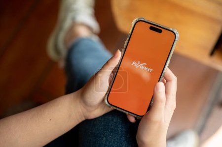 Photo for Chiang mai, Thailand - Apr 03 2024: Payoneer logo on an iPhone14 screen, a woman using the Payoneer application on her smartphone while sitting indoors. - Royalty Free Image