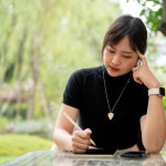 A beautiful, thoughtful Asian woman sits at an outdoor table in a beautiful garden using her digital tablet, planning or thinking about her work, working remotely. people and wireless technology