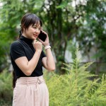 A positive, beautiful Asian woman in casual clothes talking on the phone with someone while walking in a beautiful green garden. people and wireless technology concepts