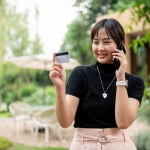 A beautiful Asian woman in casual clothes is calling her credit card or debit card call center while walking in a garden.