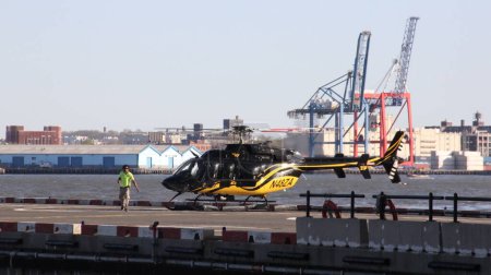 Téléchargez les photos : Bell 407 hélicoptère assis sur le sol à Downtown Heliport, Brooklyn front de mer industriel à travers East River en arrière-plan, New York, NY, États-Unis - Le 1er mai 2013 - en image libre de droit