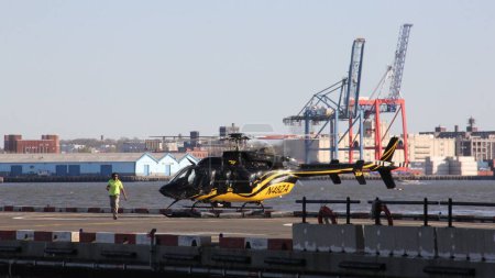 Téléchargez les photos : Bell 407 hélicoptère assis sur le sol à Downtown Heliport, Brooklyn front de mer industriel à travers East River en arrière-plan, New York, NY, États-Unis - Le 1er mai 2013 - en image libre de droit