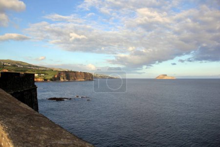 Foto de Ocean view from the Sao Sebastiao Fort, cliffs of the southern coast of Terceira Island, Cabras Islets on the horizon, sunset golden hour, Azores, Portugal - July 27, 2022 - Imagen libre de derechos