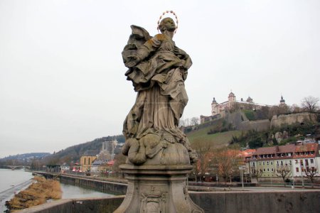 Photo for The Blessed Virgin Mary, depicted as Patrona Franconiae, statue on the Old Main Bridge, Alte Mainbruecke, Marienberg Fortress on a hill in the background, Wurzburg, Germany - January 26, 2023 - Royalty Free Image