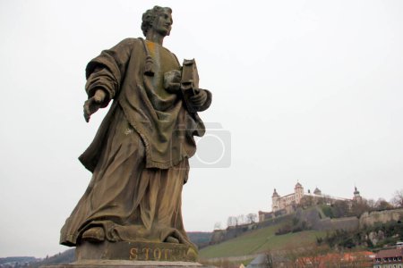 Photo for St. Totnan statue on the Old Main Bridge, Alte Mainbruecke, Marienberg Fortress on a hill in the background, Wurzburg, Germany - January 26, 2023 - Royalty Free Image