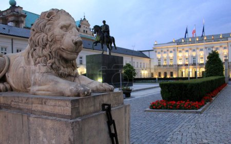 Téléchargez les photos : Lion en pierre gardant le palais présidentiel, silhouette de la statue équestre du prince Jozef Poniatowski en arrière-plan, vue dans l'illumination du soir, Varsovie, Pologne - 4 juillet 2012 - en image libre de droit