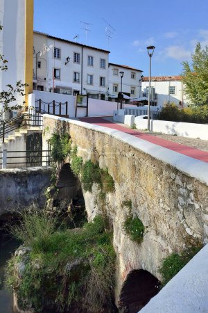 Dukes Bridge, stone footbridge across the river Almonda, running by the edge of the old town, Torres Novas, Portugal - November 25, 2023