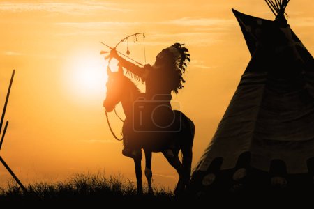 Photo for Silhouette of indian with feather headdress riding on horse back shooting arrow during sunrise or sunset. - Royalty Free Image