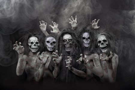 Photo for A group portrait of individuals in ghost costumes with skull faces, set against a foggy black backdrop, capturing the Halloween spirit - Royalty Free Image