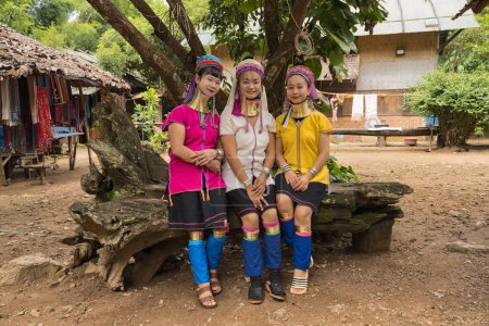 Foto de Retrato de tres mujeres Karen de cuello largo con anillos de cuello de latón con vestido tradicional estilo Karen vibrante de pie en su pueblo rústico en Pai en Mae Hong Son, Tailandia - Imagen libre de derechos