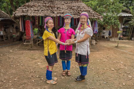Foto de Tres mujeres Karen de cuello largo con anillos de cuello de latón con vestido tradicional estilo Karen vibrante que muestra la danza Karen en su pueblo rústico en Pai en Mae Hong Son, Tailandia - Imagen libre de derechos