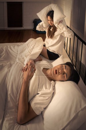 Foto de Una mujer está visiblemente frustrada mientras trata de silenciar los ronquidos perturbadores de su pareja en su cama compartida, destacando las luchas nocturnas comunes - Imagen libre de derechos