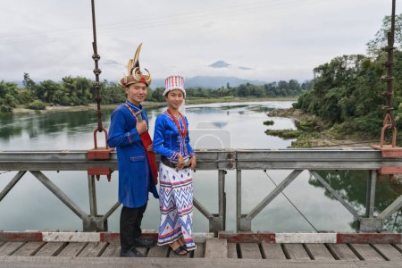 Foto de Una joven pareja Rawang, vestida con vibrante atuendo tradicional, se encuentra en el puente Kaungmulone, Putao, con el sereno río Mali Kha fluyendo suavemente en el estado de Kachin, Myanmar - Imagen libre de derechos
